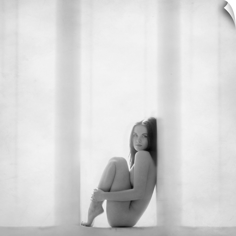 Nude woman curled up in a window frame in black and white.