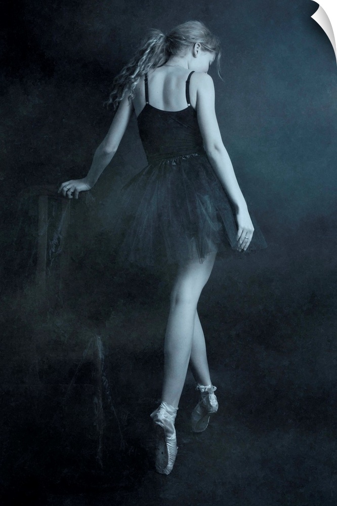 A ballerina in a black dress standing on her toes, with her back turned.