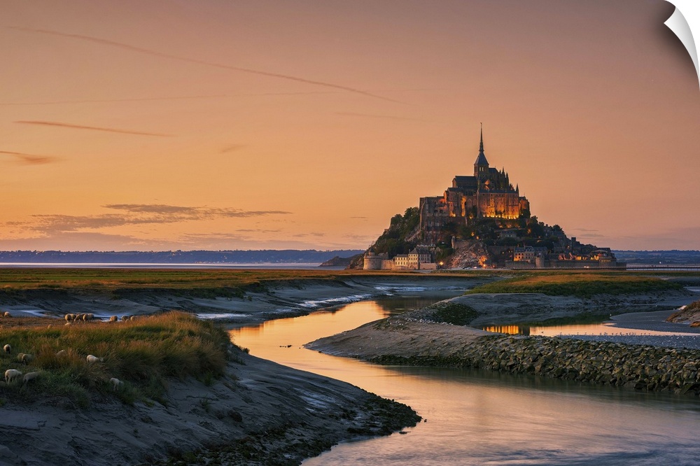 Warm landscape photograph of rivers leading to a castle on top of a hill at sunset.