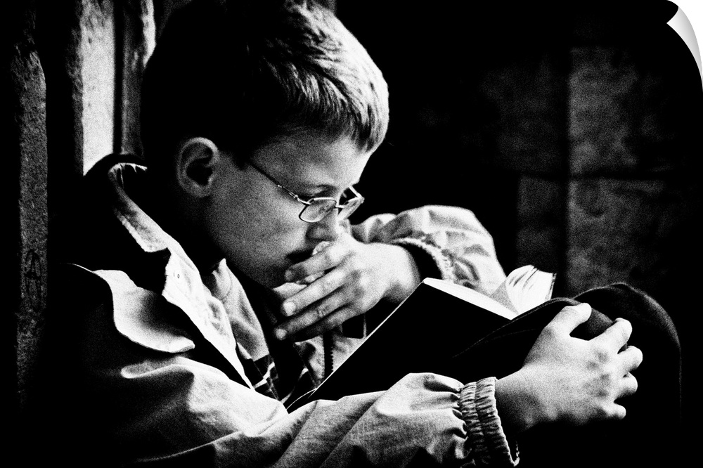 A young boy with glasses reads a book on his lap, Belgium.