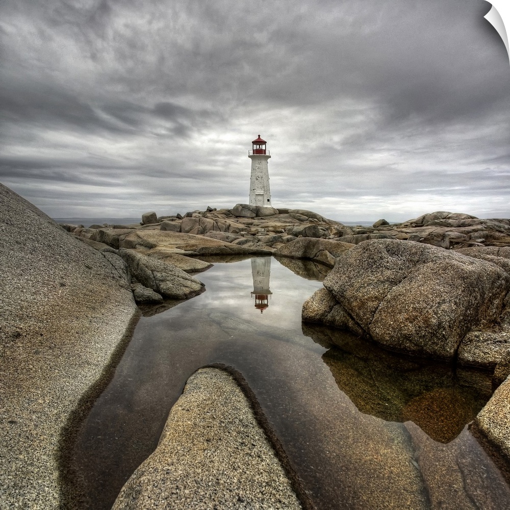 A distant Canadian lighthouse casting its reflection in a rocky tidal pool in the foreground.