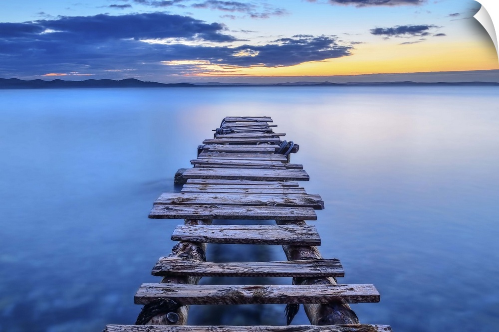 A decrepit pier jetting out over smooth blue water in Croatia.