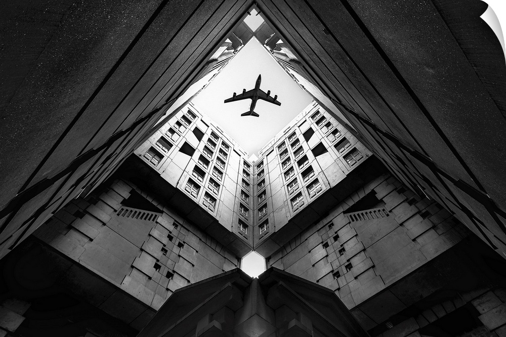 Looking up through the courtyard of a building to see an airplane flying above.