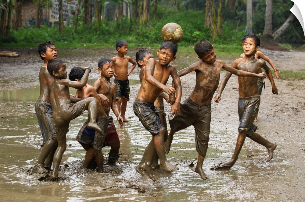 A group of young boys playing soccer in muddy water.