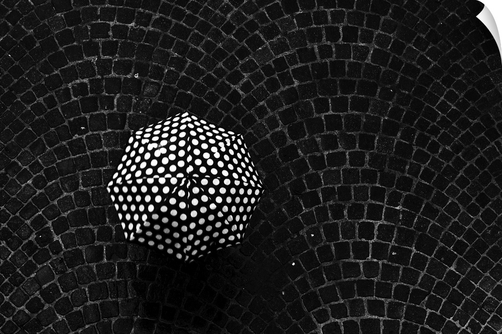 Aerial view of a polka dot umbrella held by someone standing on a cobblestone street.