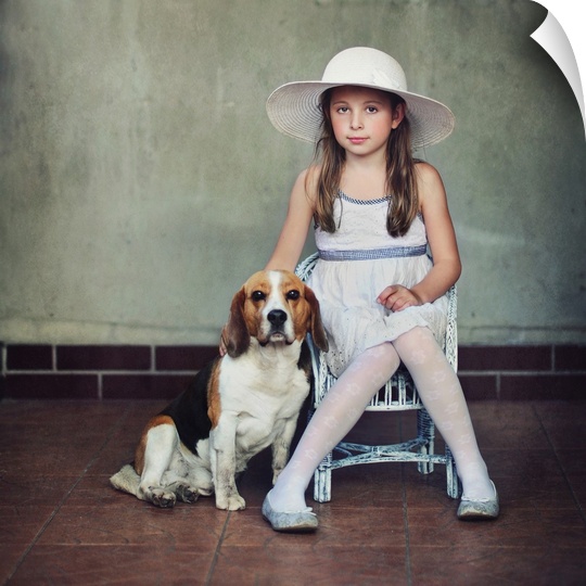 A young girl in a dress and hat sitting on a chair with her pet beagle.