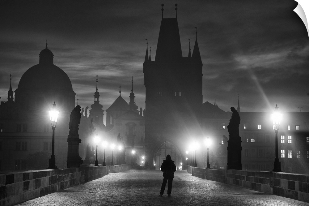 A silhouetted figure stands on a bridge at night facing the city of Prague, Czech Republic.