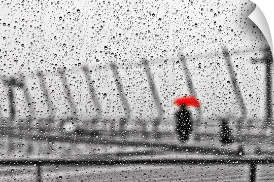 An out of focus image of a figure holding a bright red umbrella, seen through a window covered in raindrops.