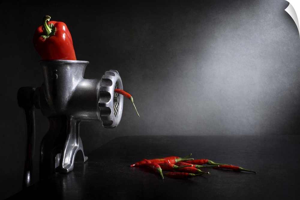 A red bell pepper in a meat grinder with small red chili peppers coming out.