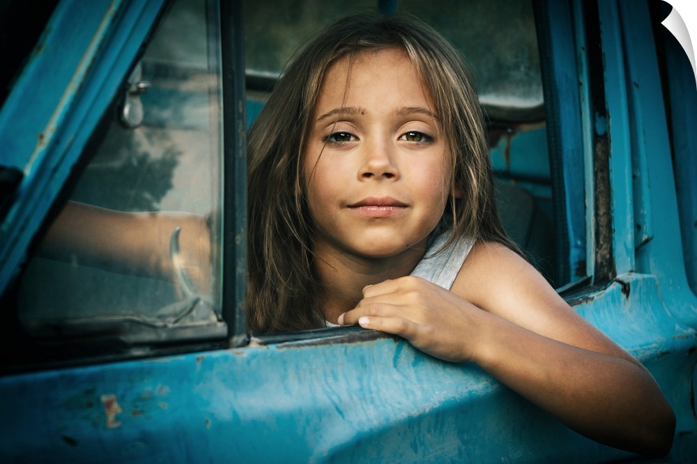 Portrait of a young girl leaning out the window of a blue car.