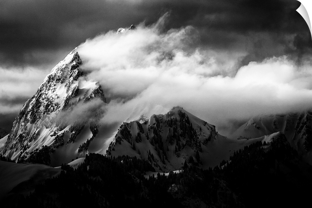 A dramatic black and white photograph of a jagged mountain peak with clouds blown around it.
