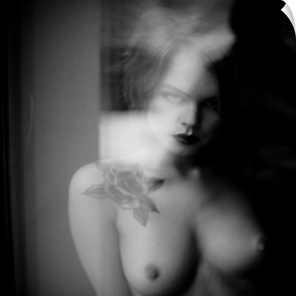 Soft focus black and white portrait of a nude woman from the chest up with a rose tattoo.