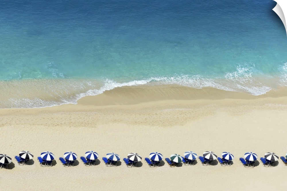Aerial view of umbrellas lined up close to the water on a beach.