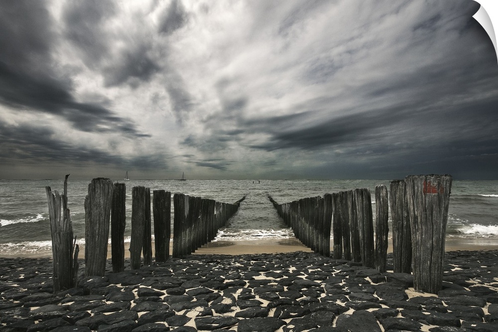 Landscape photograph of the ocean and the remains of a pier on an overcast, gloomy day.