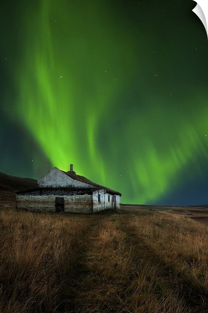 An abandoned house in a field in Iceland, with a brilliant northern lights display in the skies above.