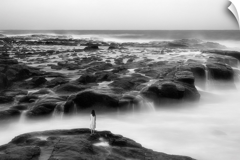 A woman standing on the edge of a rocky shore by the ocean.