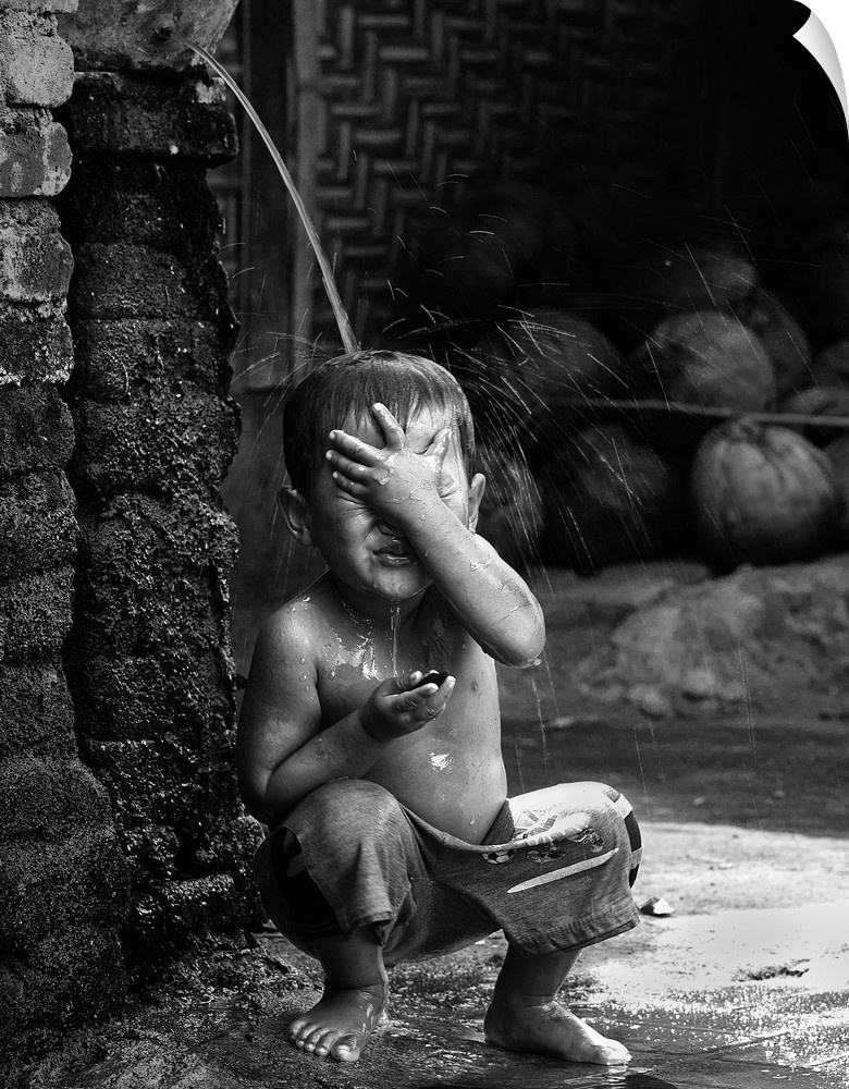 A young boy sits under a stream of water in the village of Sade, Lombok, Indonesia.