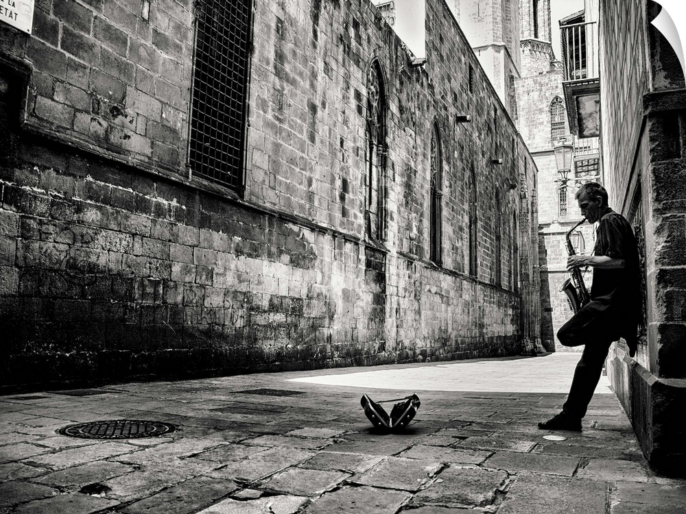 A black and white photograph of a person playing a saxophone in an alley.