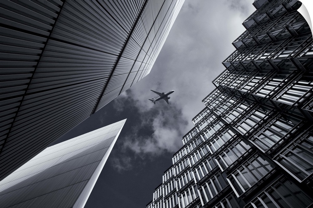 View of an airplane in the sky above tall buildings in London.