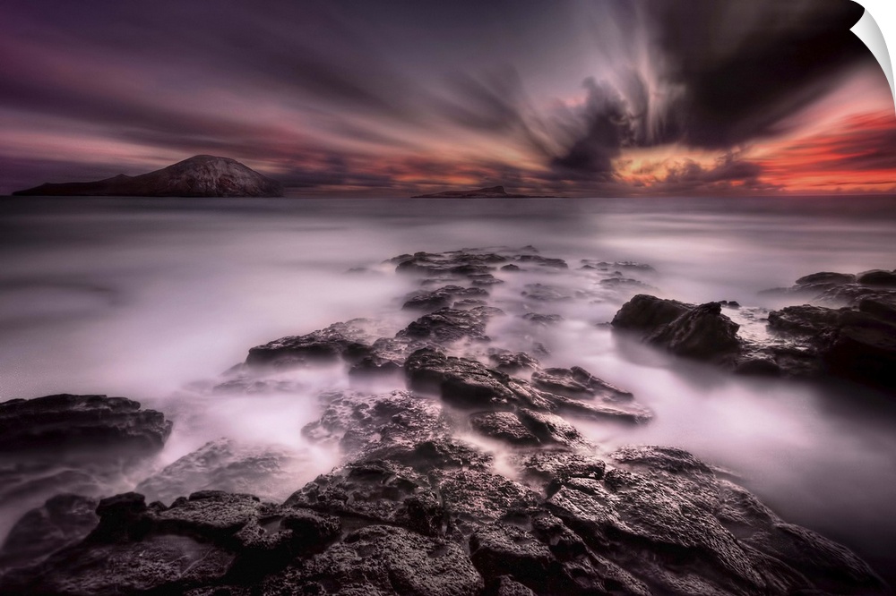 A dramatic view of a rocky coastline looking out to the sea under a blanket of intense clouds.