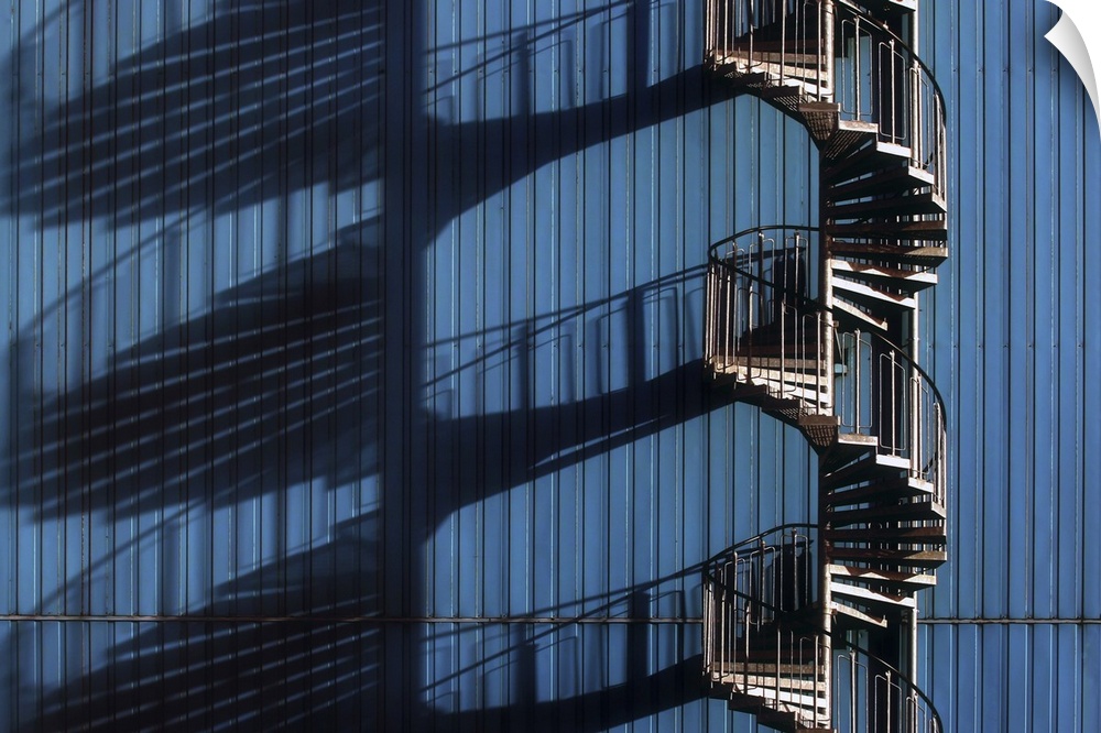 Architectural photograph of a spiral staircase casting shadows alongside a blue metal building.