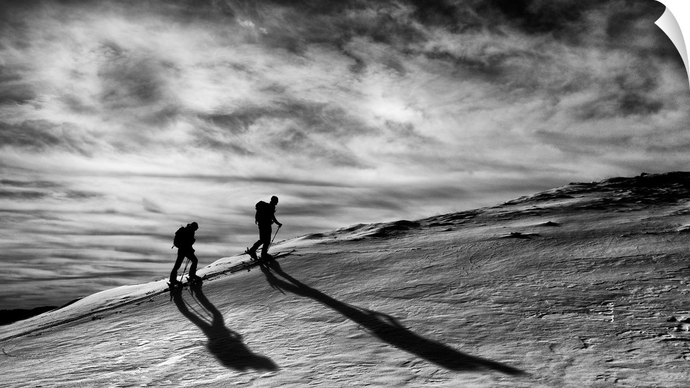 Silhouettes of two people trekking up a mountain.