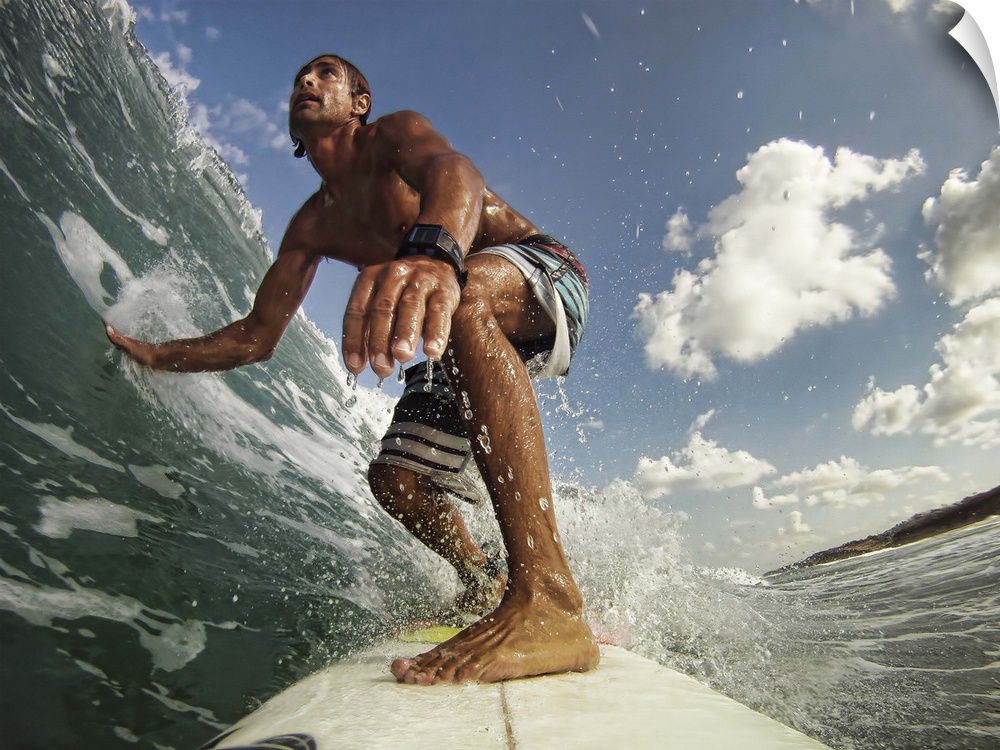 A man on a surfboard rides a wave and touches the water with his outstretched hand on a sunny day.