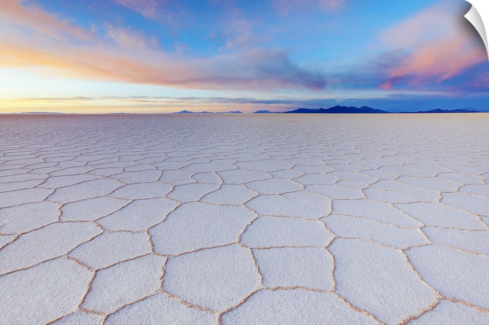 Cracked earth in the salt flats of Bolivia with pastel colors in the sky from the sunrise, Tanupa volcano in the distance.
