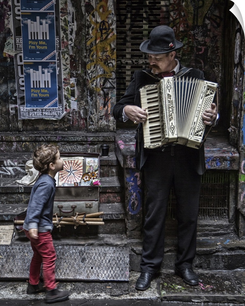 A little boy stops on a sidewalk to watch a musician play an accordion.