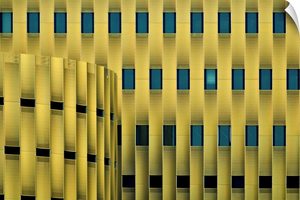 Facade of a yellow building with repeating blue windows, forming an abstract pattern.