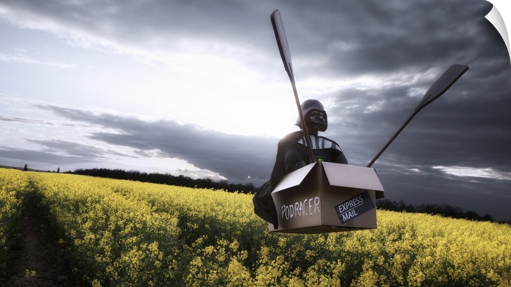 Darth Vader rides in a floating cardboard box marked "Podracer" with two large oars over a field.