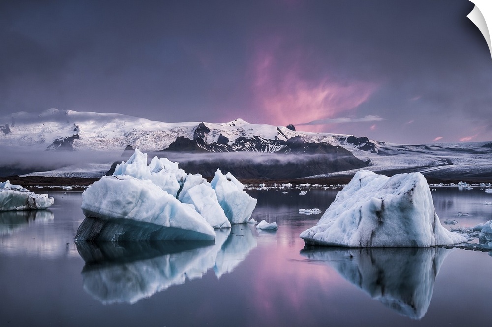 Large glaciers in the water with snowy mountains in the distance under a pastel-colored sky, Jokulsarlon, Iceland.