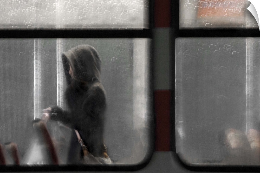 A women wearing a hood walking down the aisle of a train seen through the window.