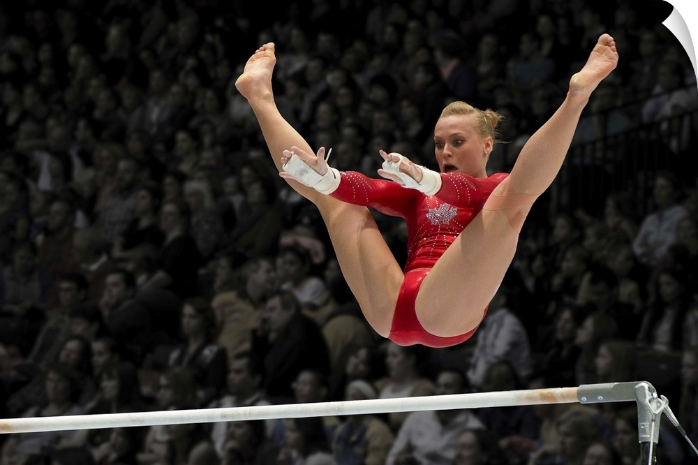 A female gymnast flies over the high bar with her legs raised up, arms outstretched ready to grab the bar.