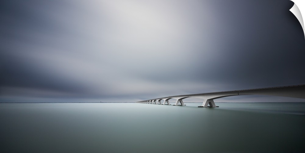 An infinite looking bridge spans a smooth flat green river under a dark blue sky.