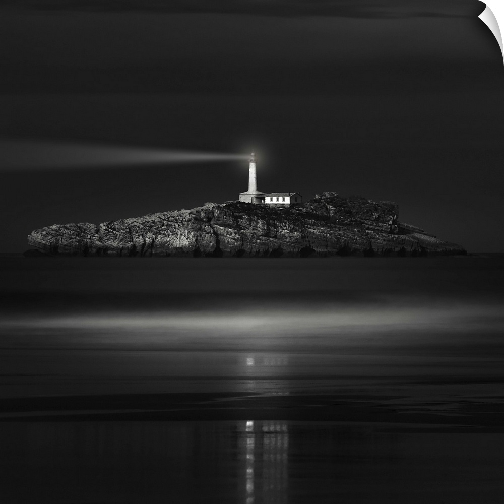 A lighthouse on a rocky island in the ocean shines a bright light into the night.