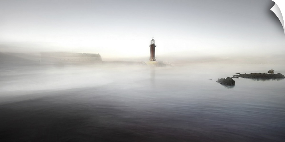 A lighthouse on a pier partially obscured by mist, making it appear as though it is rising from the ocean.