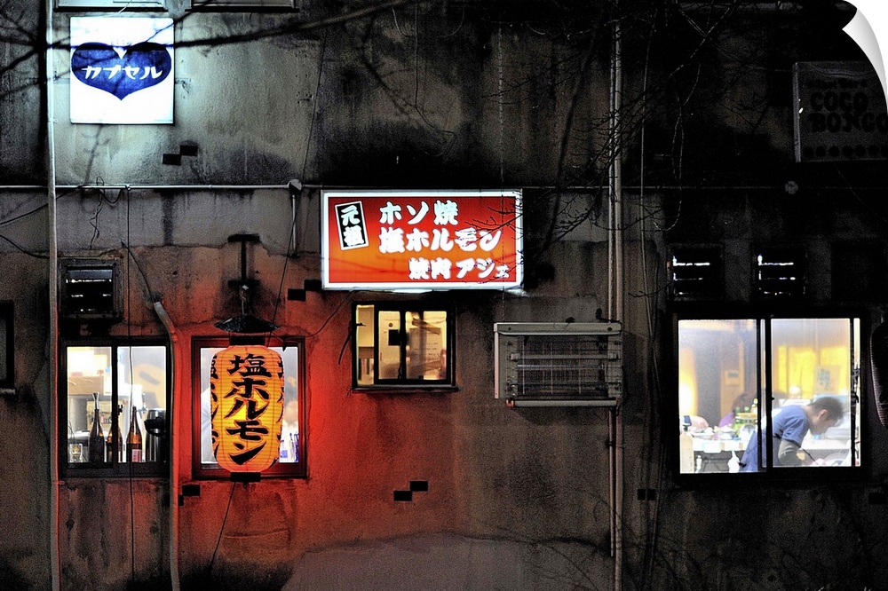 A wall with lit up street signs and windows on the side of a building in Kyoto, Japan.