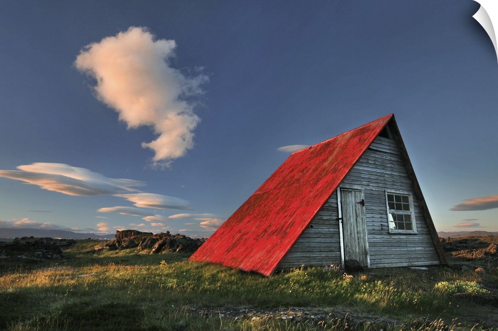a wooden hut in Iceland with a bright red roof, seen at sunset.