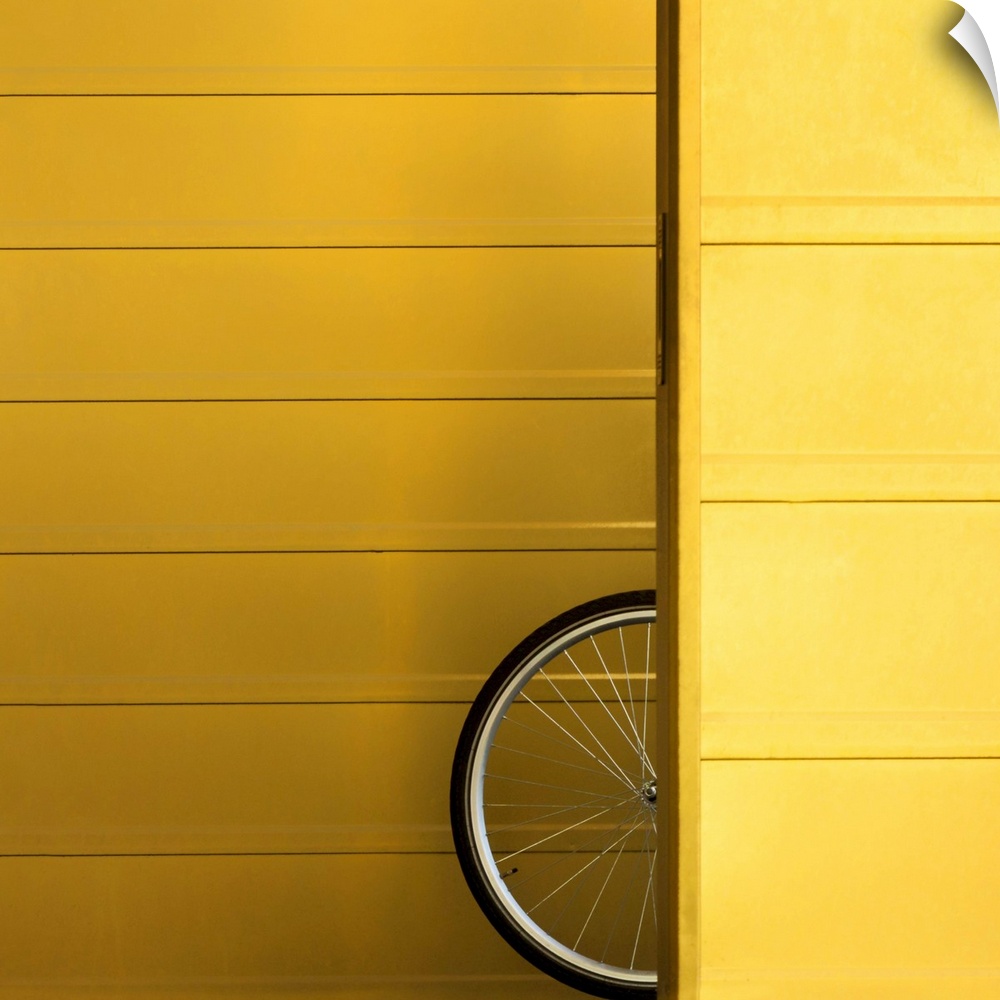 A bicycle wheel poking out from behind a yellow wall.