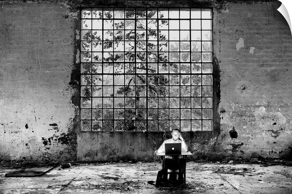 Conceptual photo of a man sitting at a desk in an abandoned building looking at a laptop.