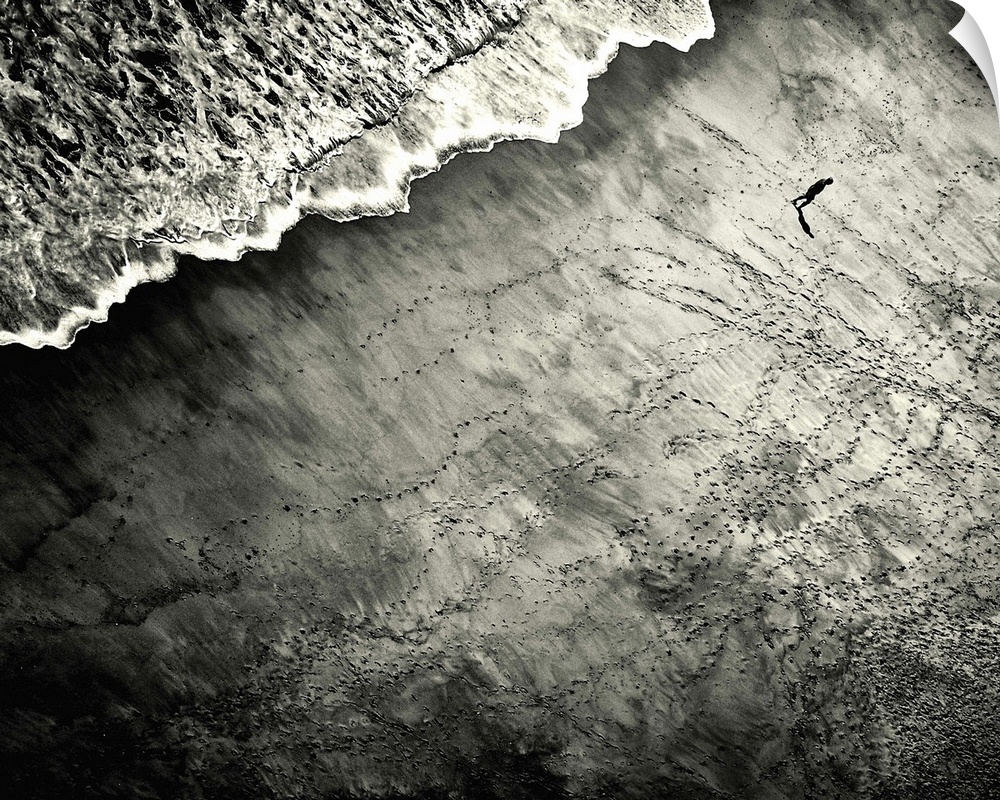Aerial view of a person on a beach looking at all the footprints created by other people.