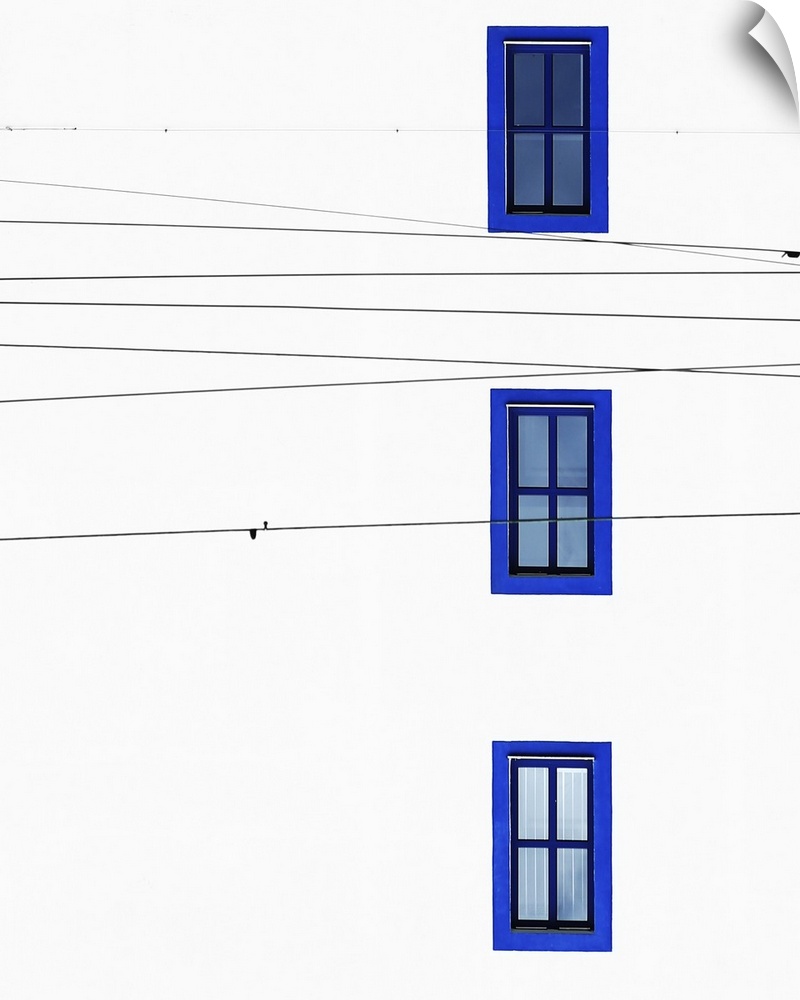 The wall of a building with three windows with blue frames and intersecting power lines.