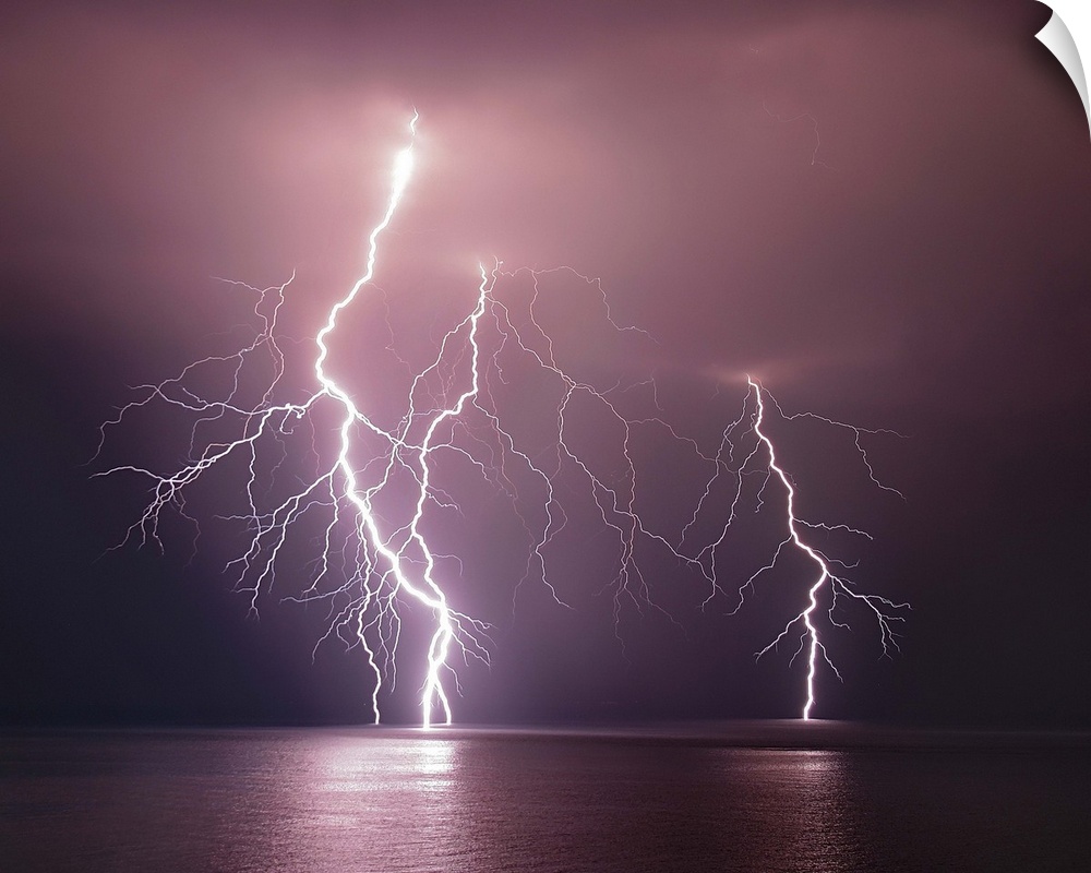 Dramatic image of three lightning bolts striking the ocean at night.