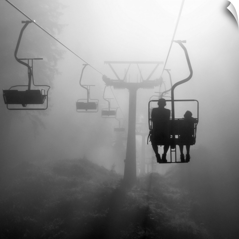 Two silhouetted people on a chairlift heading into the dense fog.