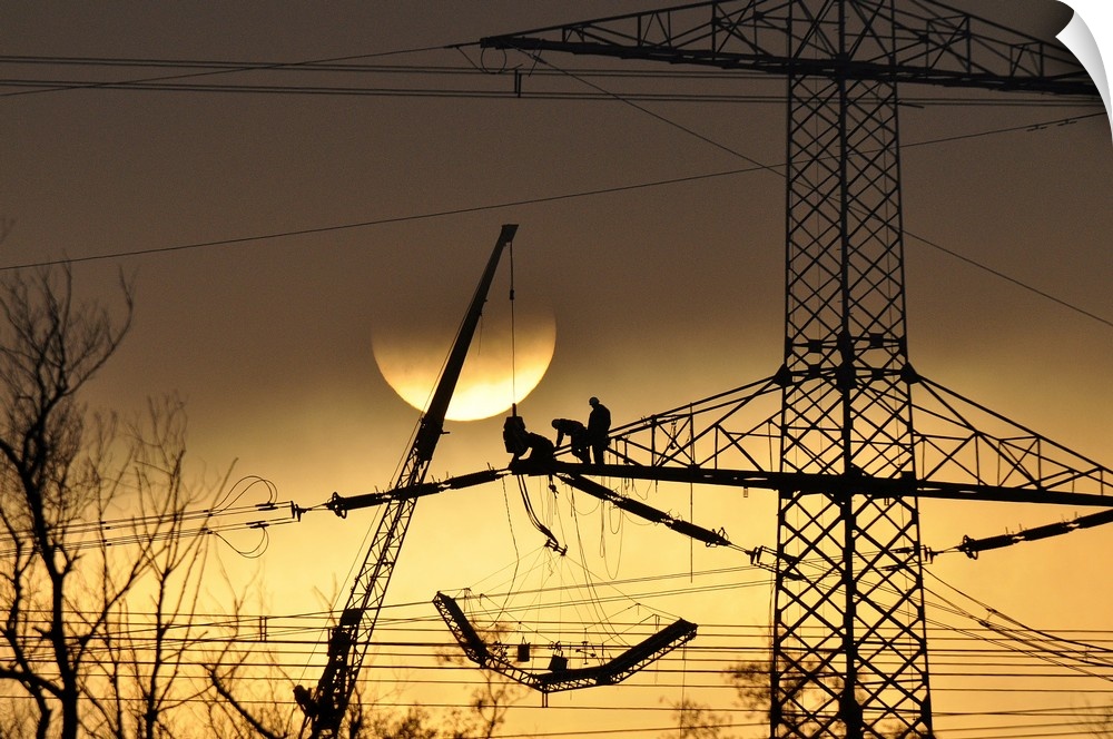 Silhouette of people working on a large electrical pylon with the sun setting in the background.
