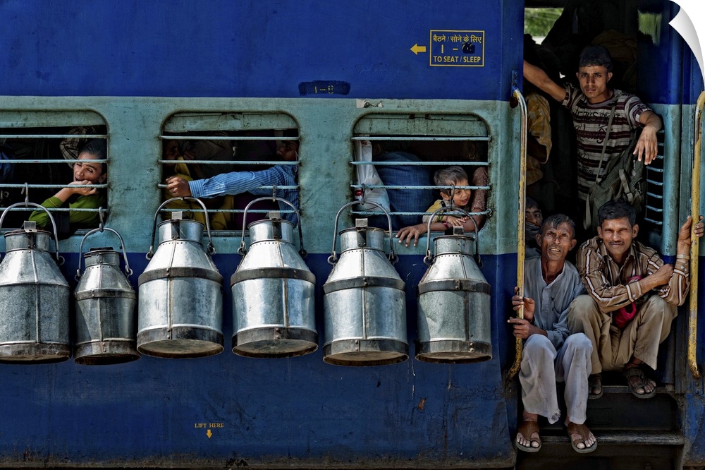 Passengers in the door and windows of a train in India, with milk cans hanging on the sides.