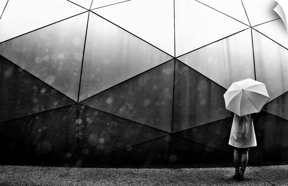 A person with an umbrella standing in the street near a large geometric structure.