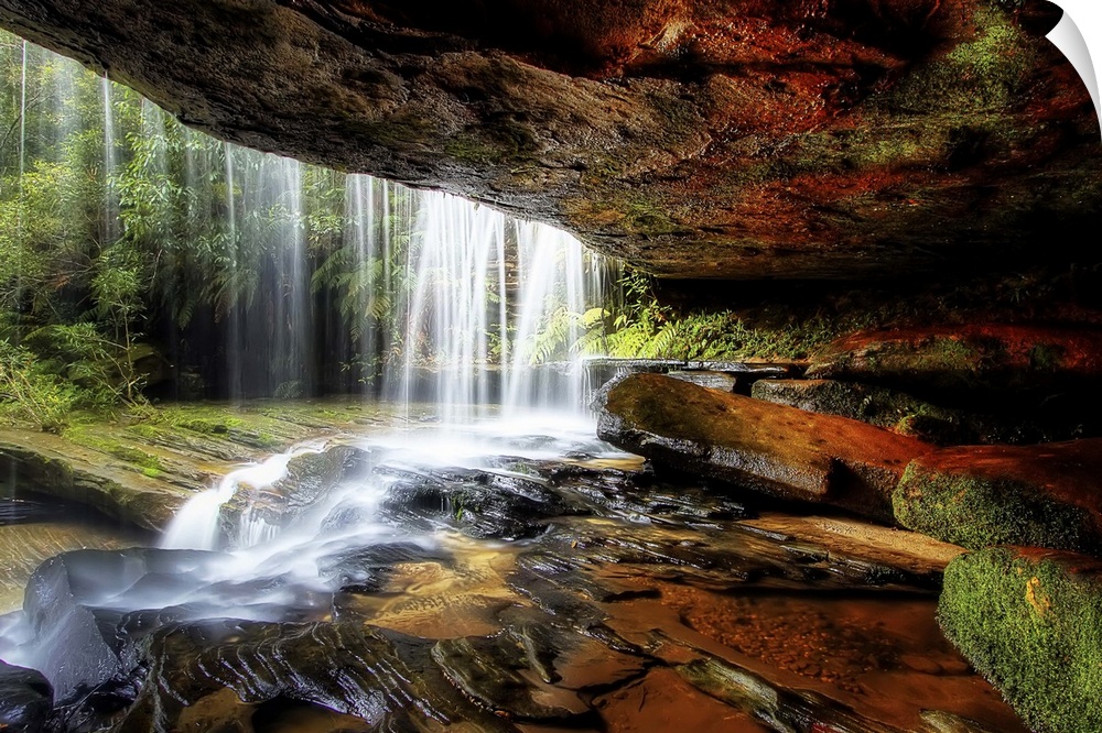 A cave behind a waterfall with wet stones and moss.