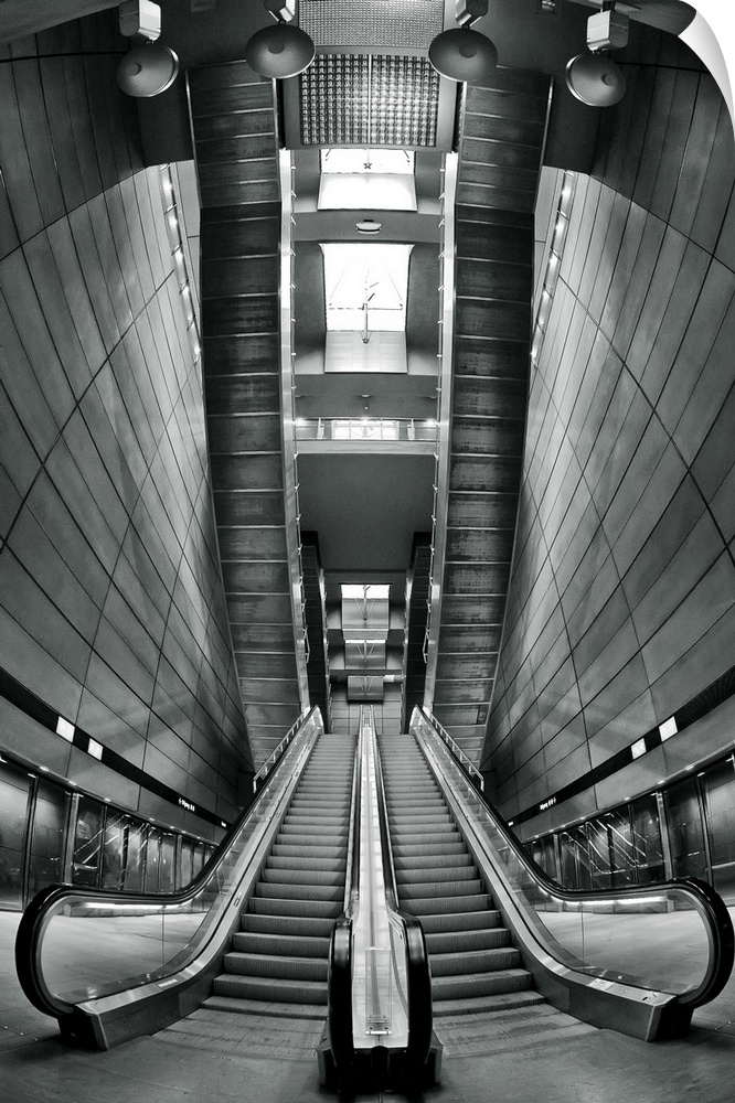 Black and white image of escalators in a station, with a view of the skylights in the ceiling.